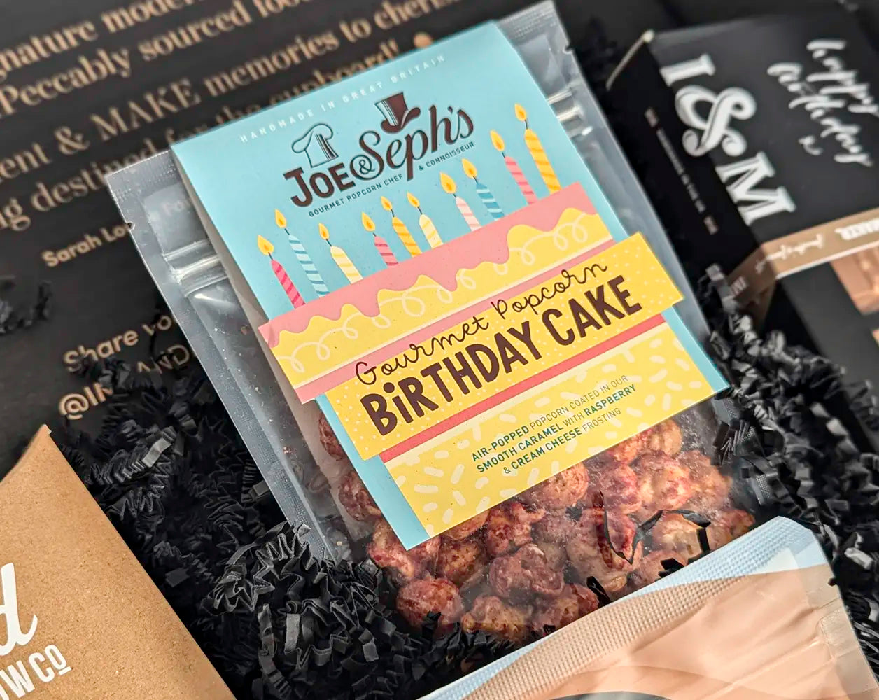 Packaged gourmet popcorn with 'Birthday Cake' flavor on a black textured background