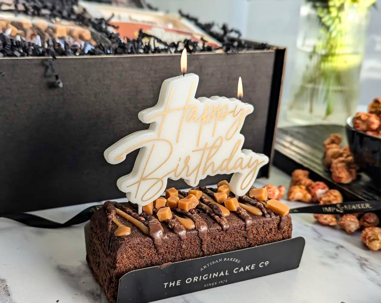 Birthday cake with 'Happy Birthday' candle and chocolate decorations on a marble surface.