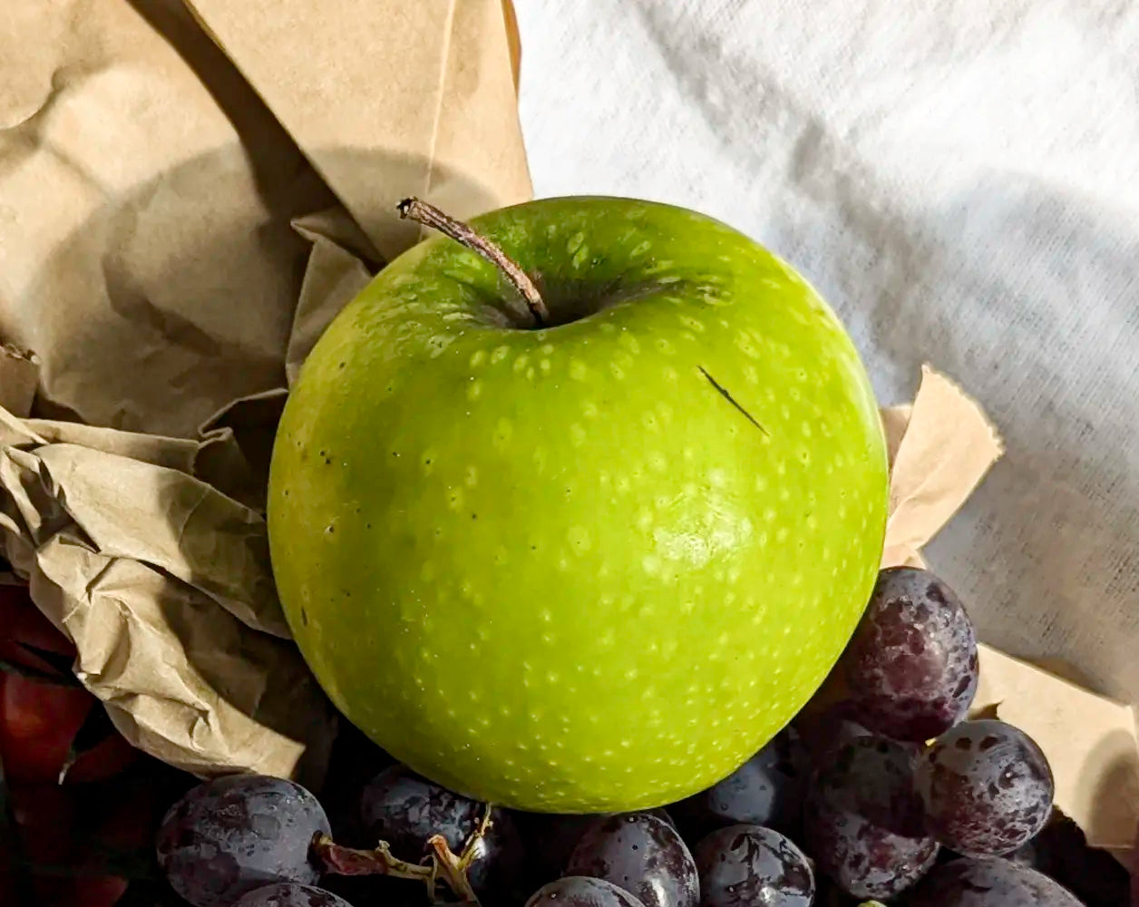 Green apple on a bed of purple grapes with a white cloth background