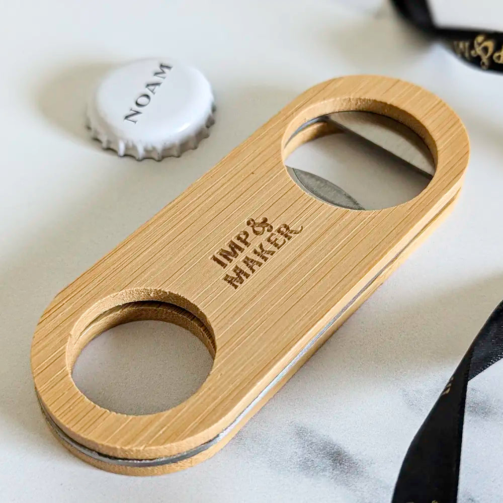 Wooden bottle opener with 'Imp & Maker' branding on a marble surface.