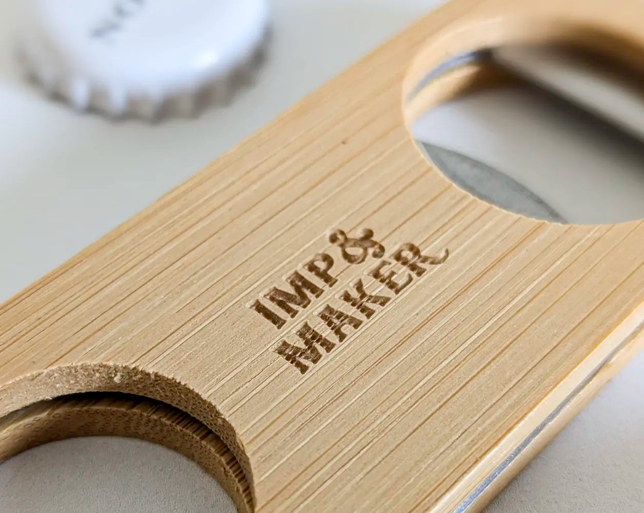 Wooden bottle opener with 'Imp & Maker' branding on a marble surface.