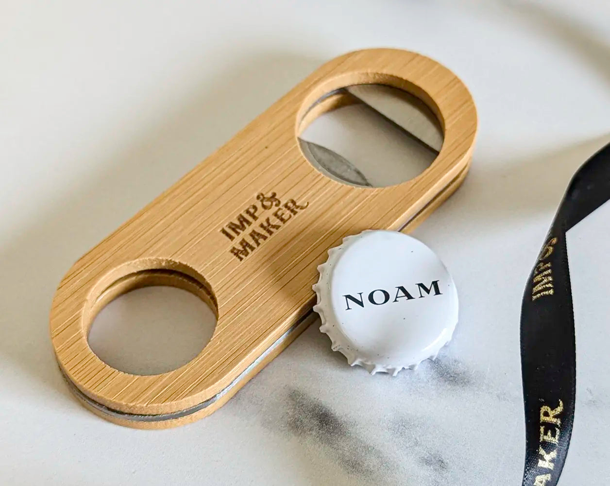 Wooden bottle opener with 'Imp & Maker' branding on a marble surface.