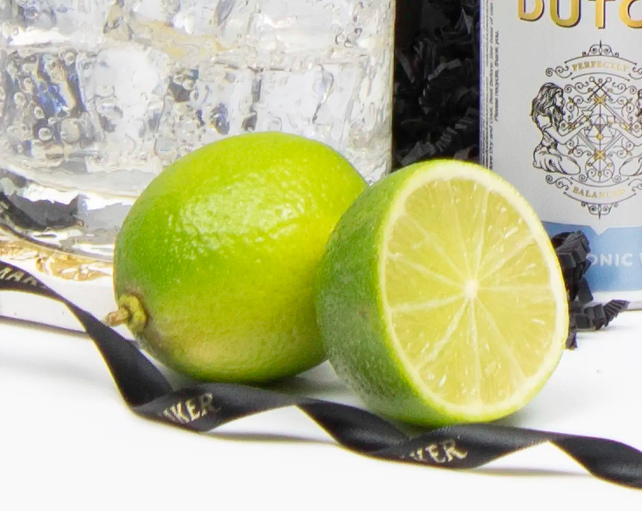 Two limes, one whole and one sliced, with a bottle of gin in the background.