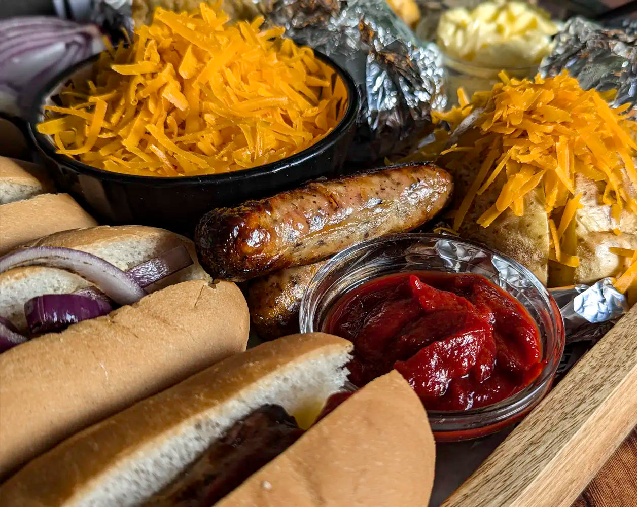 Assorted food items including buns, sausages, cheese, and condiments on a wooden surface.