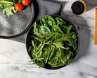 Bowl of fresh greens on a marble surface with a bottle of olive oil.