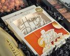 'Happy Birthday' candle in a decorative box with gold text.