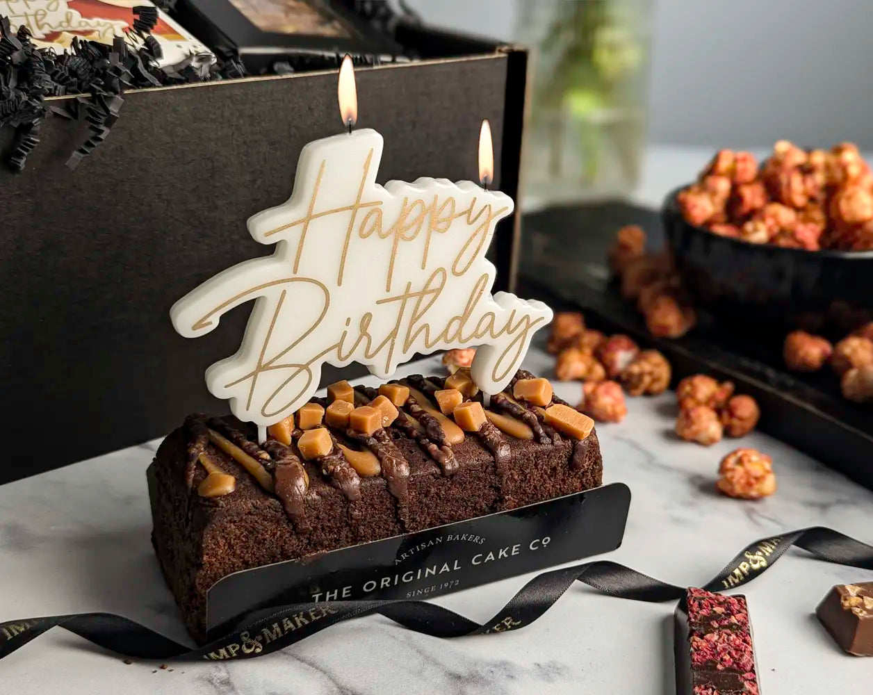 Birthday cake with 'Happy Birthday' candle and chocolate cake on a marble surface.