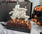 Small birthday cake with 'Happy Birthday' candle and visible brand name on a marble surface.