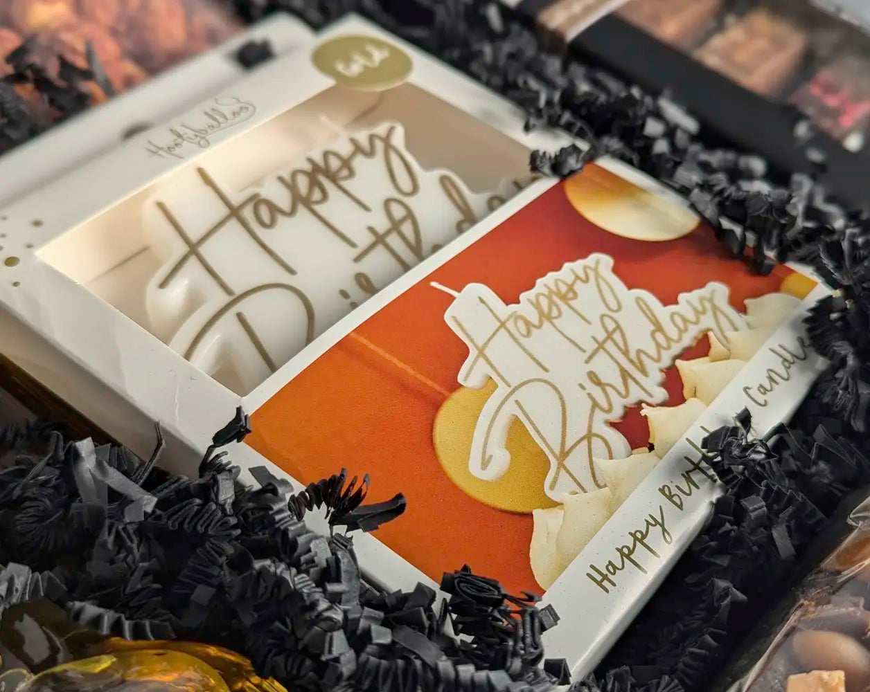 Close-up of a 'Happy Birthday' candle with decorative elements on a black textured background.