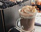 Glass mug with layered hot chocolate and cream with chocolate shavings on a marble surface