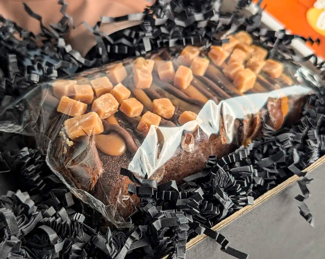 Packaged cake with caramel pieces on a bed of black crinkle paper