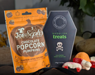 Joe Seph's chocolate popcorn pumpkins packaging and a coffin-shaped bag of 'Ghoulish Treats' on a dark surface.