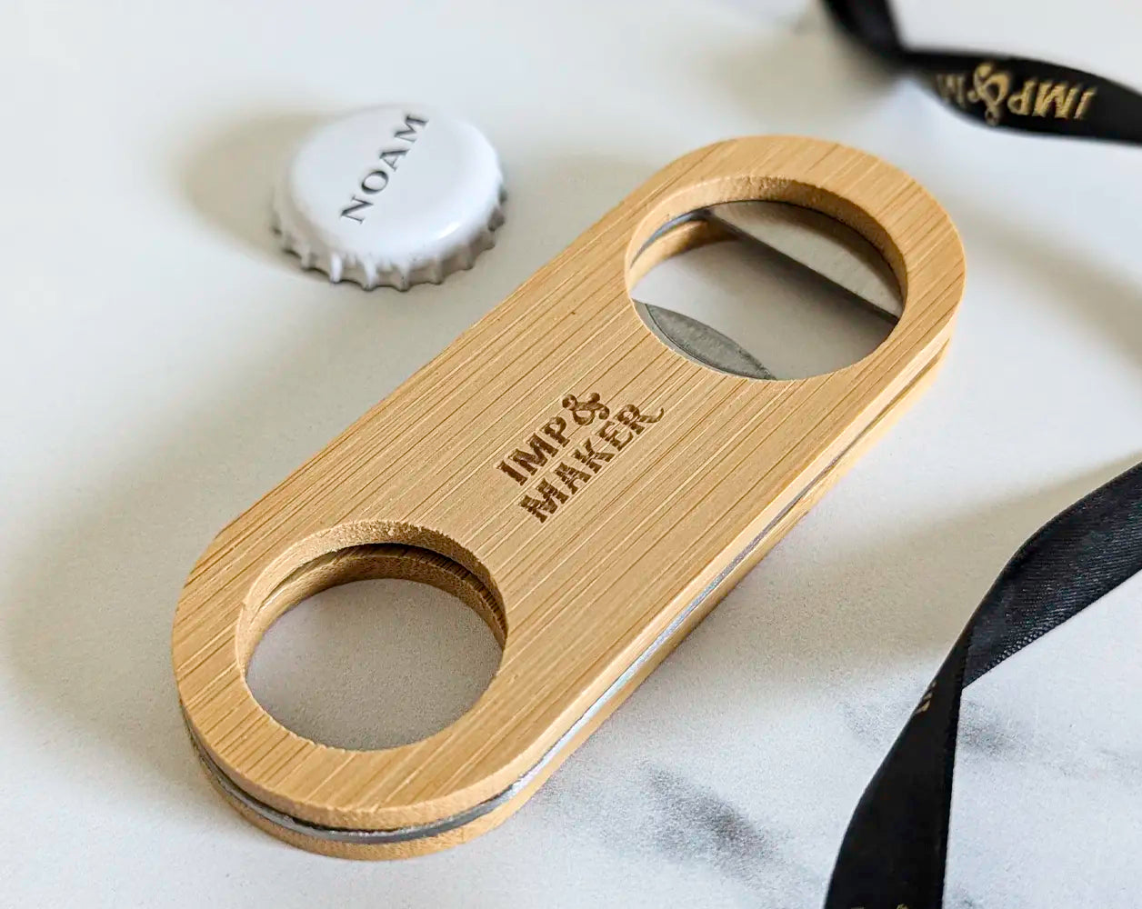 Wooden bottle opener with 'Imp & Maker' branding on a marble surface.