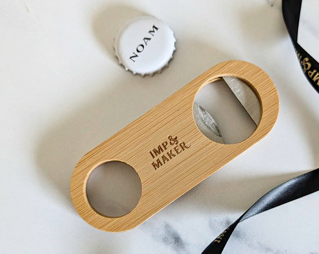 Wooden bottle opener with 'IMP & MAKER' branding on a marble surface.