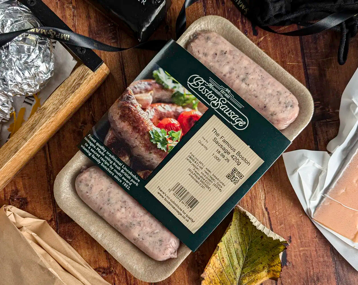 Boston Sausage Sausages in packaging on a wooden surface with ingredients and decorative ribbon.