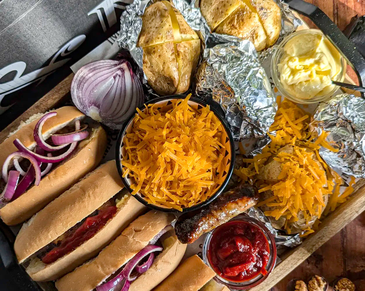 Assorted food items including buns, cheese, onions, and condiments on a wooden tray.