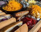 Assorted food items including buns, sausages, cheese, and condiments on a wooden surface.